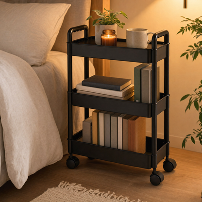 Black 3-tier rolling cart used as a bedside table with books, a mug and a candle