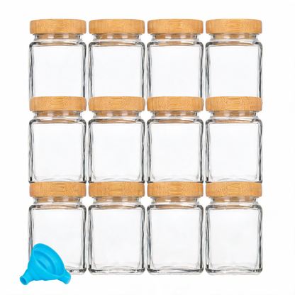 Twelve glass spice jars with bamboo lids and funnel on white